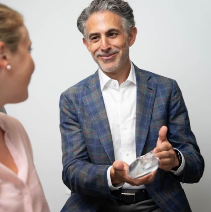 Dr. Samson holding a silicon breast implant while discussing breast augmentation with a patient